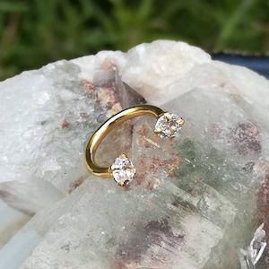 May include: Gold horseshoe ring with two clear round gemstones.