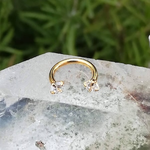 May include: Gold-toned circular barbell with two clear cubic zirconia stones on each end.