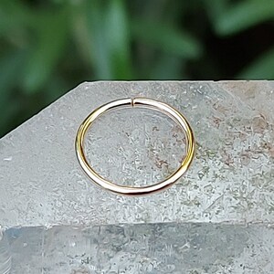 May include: A gold nose ring hoop, a type of body jewelry, is shown on a white crystal surface.