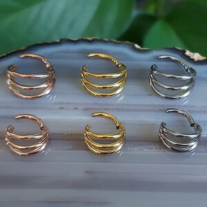 May include: Six nose rings with a triple hoop design. The rings are available in gold, silver, and rose gold.