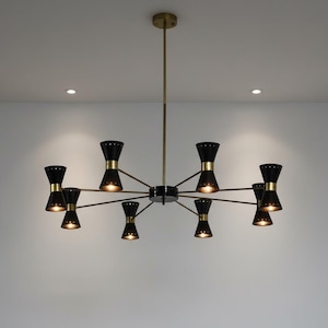 May include: A contemporary chandelier featuring eight black, hourglass-shaped shades with gold-coloured bands. The fixture has a central black hub, brass-coloured arms, and a central rod. The lights are on, illuminating the room.
