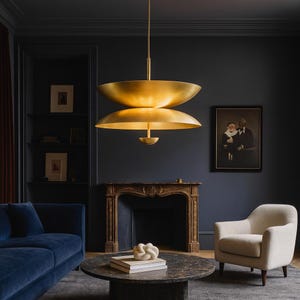 May include: A contemporary gold pendant light with two tiers suspended from the ceiling. The room features dark blue walls, a blue velvet sofa, and a marble coffee table. A painting and a fireplace are also visible, creating a luxurious atmosphere.