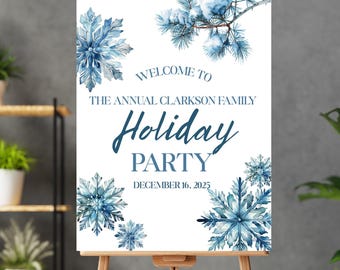 May include: A wooden easel displays a white sign with blue snowflake and floral watercolor designs. The sign reads "Welcome to The Annual Clarkson Family Holiday Party December 16, 2025."