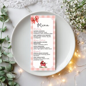 May include: A menu card with a pink gingham border and a red bow at the top. The menu lists starters, main entrees, and desserts, including Caprese skewers, herb-roasted chicken, and vanilla bean cupcakes. The card is on a white plate.