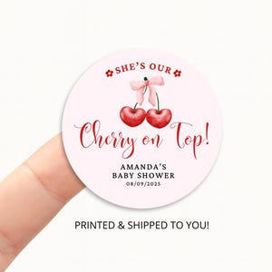 May include: A circular, pale pink sticker featuring red text and a watercolour illustration of two cherries with a pink bow. The text reads "She's Our Cherry on Top!" and "Amanda's Baby Shower 08/09/2025."