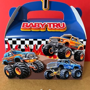 Puede incluir: Una caja de regalo azul con asa, con ilustraciones de monster trucks y el texto "BABY TRU". La caja está decorada con banderas a cuadros y el número "1".