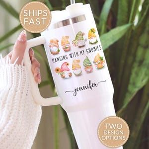 May include: A white stainless steel tumbler with a handle and a straw, featuring a colorful graphic of eight small gnomes and the text "HANGING WITH MY GNOMIES" printed above the name "jennifer" in a black cursive script font.