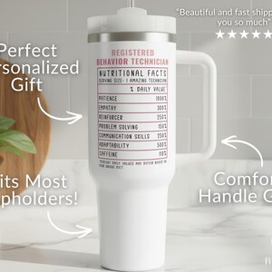 Pode incluir: Caneca branca com al&ccedil;a, com o texto "REGISTERED BEHAVIOR TECHNICIAN" e um r&oacute;tulo de "Informa&ccedil;&atilde;o Nutricional". A caneca tem uma tampa branca e uma pega confort&aacute;vel. O texto "Fits Most Cupholders!" tamb&eacute;m &eacute; vis&iacute;vel.