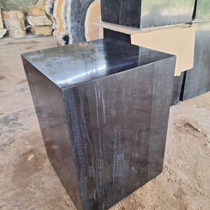 Puede incluir: Una mesa auxiliar cuadrada de madera oscura con un acabado brillante. La mesa tiene un diseño angular único y un color oscuro intenso con vetas de madera visibles. La mesa es probablemente para uso en interiores.