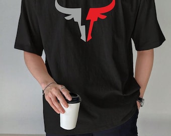 May include: Black t-shirt featuring a stylized bull graphic in gray and red. The shirt has a relaxed fit and short sleeves. The person is holding a white coffee cup with a black lid.
