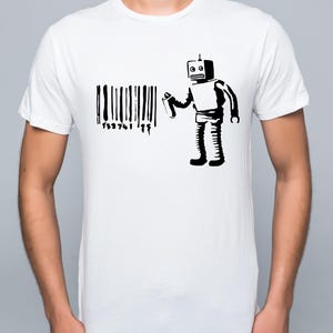 Peut inclure: T-shirt blanc avec un motif noir d'un robot pulvérisant un code-barres avec une bombe aérosol. Le robot a une tête carrée et porte un costume. Le code-barres porte les chiffres "132741 99".