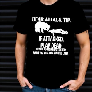 Peut inclure: T-shirt noir avec texte et graphiques blancs. Le texte se lit comme suit : « CONSEIL D'ATTAQUE D'OURS : SI ATTAQUÉ, FAITES LE MORT. CE SERA UN BON ENTRAÎNEMENT POUR QUAND VOUS MOURREZ QUELQUES MINUTES PLUS TARD. » Le graphique montre un ours et une personne.