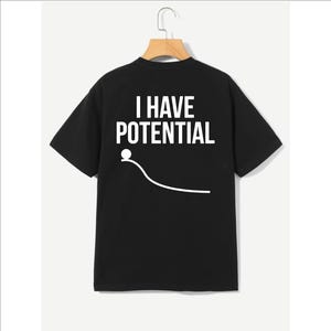 Könnte beinhalten: Schwarzes T-Shirt mit dem weißen Text "I HAVE POTENTIAL" und einer weißen Grafik eines Balls, der eine Rampe hinunterrollt. Die Grafik enthält einen weißen Punkt und eine gebogene Linie.