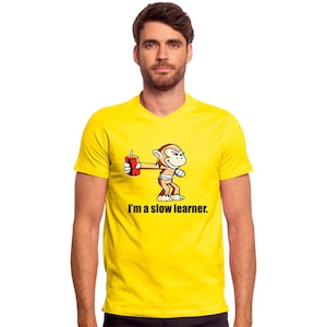 May include: Yellow V-neck t-shirt featuring a cartoon monkey holding a red soda can. The monkey has a mischievous expression. The text "I'm a slow learner" is printed below the monkey graphic.