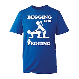 Puede incluir: Camiseta azul real con texto y gráfico blancos. El texto dice "BEGGING FOR A PEGGING" encima de una ilustración estilizada de dos figuras. La camiseta está hecha de un material suave.