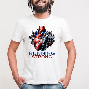 Puede incluir: Camiseta blanca con un gráfico detallado de un corazón humano en rojo y azul, integrado con componentes mecánicos. El texto "RUNNING STRONG" está impreso debajo del corazón en azul y rojo.