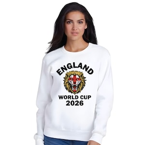 May include: White sweatshirt featuring the text "ENGLAND" above a lion graphic with the England flag colors. Below the lion is the text "WORLD CUP 2026". The sweatshirt is a crew neck style.