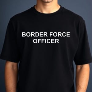 Könnte beinhalten: Schwarzes T-Shirt mit dem weißen Text "BORDER FORCE OFFICER" auf der Brust. Das T-Shirt hat kurze Ärmel und einen Rundhalsausschnitt. Das Bild ist eine mittlere Aufnahme des T-Shirts.