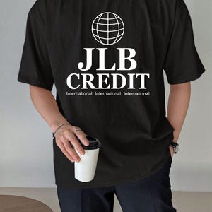 Könnte beinhalten: Schwarzes T-Shirt mit weißer Weltkugel-Grafik und dem Text "JLB CREDIT" über "International International International". Lässiger Stil.