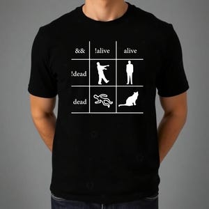 May include: A black short-sleeved t-shirt featuring a white grid graphic. The grid contains the text &&, !alive, alive, !dead, and dead, alongside white silhouettes of a zombie, a standing person, a chalk outline, and a sitting cat.