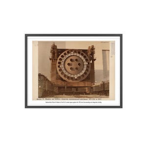 Peut inclure: Photographie vintage encadrée d'une grande structure industrielle circulaire, possiblement un composant de fusée, avec de multiples ouvertures. Deux trains encadrent la structure. L'image contient du texte en bas, sur fond clair.