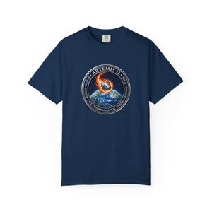 May include: Navy blue t-shirt featuring a circular graphic of a fiery object descending towards Earth. The graphic includes the text "ARTEMIS II SPLASHDOWN APRIL 10 2026" and the names of the crew members. A classic crew neck tee.