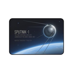 Könnte beinhalten: Ein schwarzes rechteckiges Mousepad mit einer Illustration von Sputnik-1, dem ersten künstlichen Satelliten, vor dem Hintergrund von Weltraum und Erde. Der Text lautet "SPUTNIK-1" und enthält Details über Masse und Durchmesser des Satelliten (58 cm).