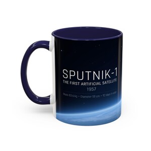 May include: A white ceramic mug with a navy blue interior and handle. The mug features the text "SPUTNIK-1" with details about the first artificial satellite, including its mass of 184.3 pounds, a diameter of 22.8 inches, and 92 days in orbit.