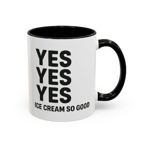 Può includere: Tazza in ceramica bianca con interno e manico neri. La tazza presenta la parola "YES" impilata tre volte in lettere nere in grassetto, con "ICE CREAM SO GOOD" stampato sotto.
