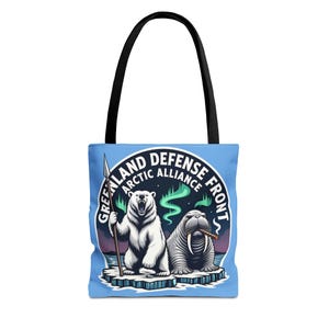 Puede incluir: Un bolso tote azul claro con asas negras. El bolso presenta un emblema circular con un oso polar sosteniendo una lanza y una morsa fumando un cigarro. El texto dice "GREENLAND ARCTIC DEFENSE FRONT".