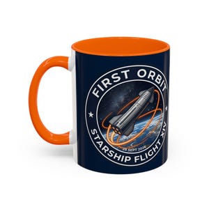 Pode incluir: Uma caneca de cerâmica azul-escura com asa e interior laranja brilhante. O exterior apresenta um gráfico circular de um foguetão prateado em órbita da Terra com trajetórias de voo cor de laranja e o texto FIRST ORBIT STARSHIP FLIGHT XIV 28 SEPT 2026.