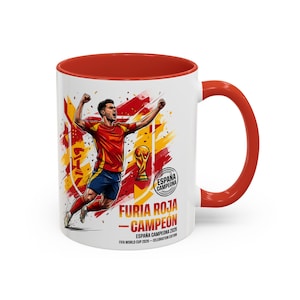 May include: A white ceramic mug with a red interior and handle, featuring a graphic of a soccer player celebrating next to a trophy. The text reads "FURIA ROJA - CAMPEÓN", "ESPAÑA CAMPEONA 2026", "FIFA WORLD CUP 2026 - CELEBRATION EDITION", and "ESPAÑA CAMPEONA".