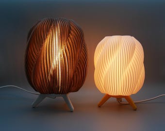 Può includere: Due lampade decorative con un design unico e strutturato. Una lampada è di colore marrone caldo, l'altra bianca. Entrambe le lampade hanno una forma arrotondata e sono sostenute da tre piccole gambe. Le lampade sono accese, emettendo una luce soffusa.