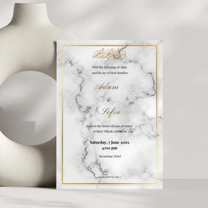 May include: A wedding invitation with a marble effect background and gold detailing. The invitation features the names "Adam" and "Sofia", the date, time, and venue. The text is in gold, and the invitation is framed with a gold border.