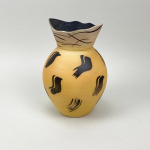 May include: A decorative ceramic vase with a rounded body and a flared, wavy rim. The vase is painted in a warm yellow with black brushstroke designs. The rim is dark blue with a silver accent.