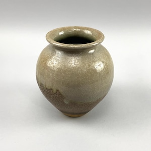 May include: A small, round, ceramic vase with a light brown glaze. The vase has a speckled texture and a slightly uneven rim.