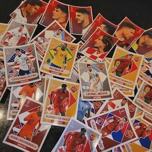 Op de afbeelding: Een verzameling voetbal trading cards met afbeeldingen van spelers en namen. De kaarten hebben een rood, wit en goud kleurenschema. Sommige kaarten zijn gemarkeerd als "Rookie" of "Legend".