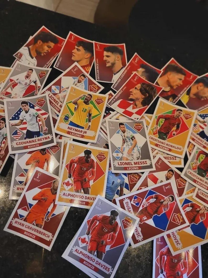 Op de afbeelding: Een verzameling voetbal trading cards met afbeeldingen van spelers en namen. De kaarten hebben een rood, wit en goud kleurenschema. Sommige kaarten zijn gemarkeerd als "Rookie" of "Legend".