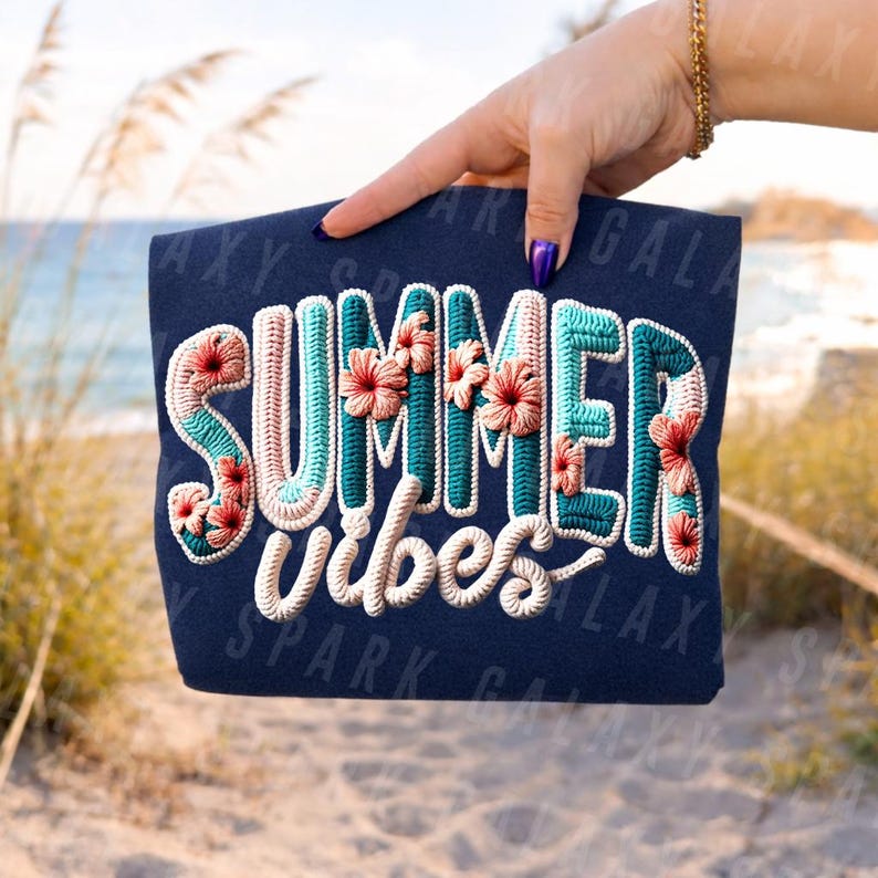 May include: Navy blue tote bag with the words "SUMMER VIBES" embroidered in white, teal, and coral. The word "SUMMER" is decorated with coral hibiscus flowers. The bag is held up against a beach background.