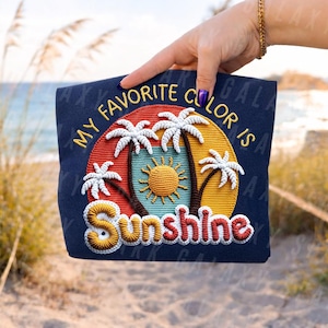 May include: Navy blue tote bag with an embroidered design featuring palm trees, a sun, and the text "MY FAVORITE COLOUR IS SUNSHINE" in yellow and red. The bag is held up by a hand.