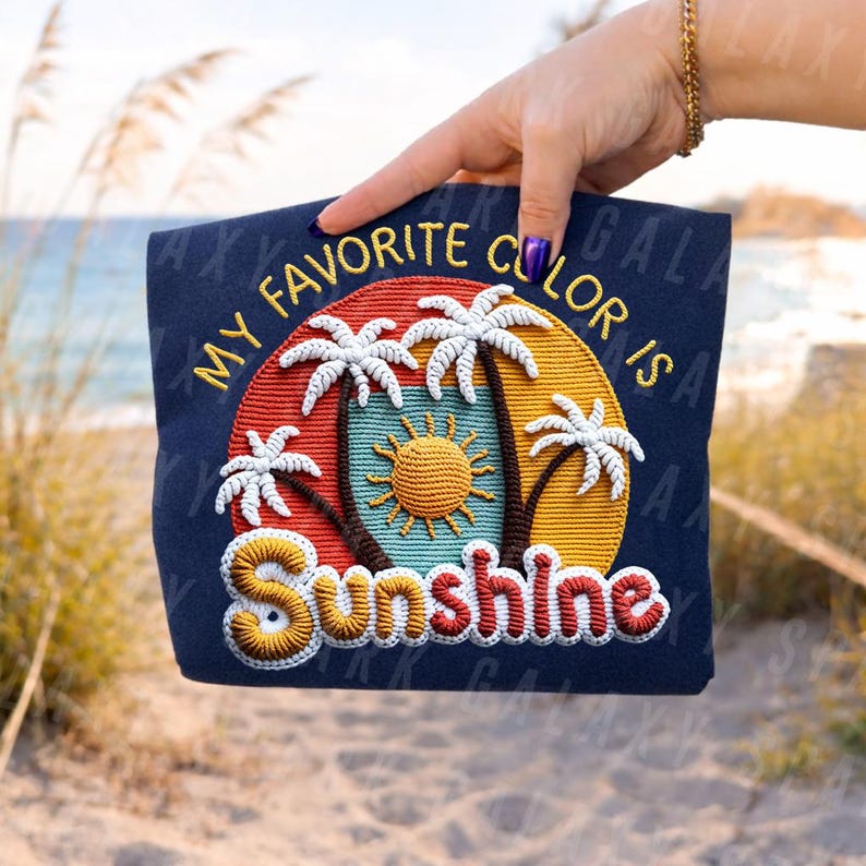 May include: Navy blue tote bag with an embroidered design featuring palm trees, a sun, and the text "MY FAVORITE COLOUR IS SUNSHINE" in yellow and red. The bag is held up by a hand.