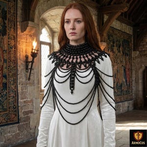 Peut inclure: Un plastron noir perlé avec un design en forme de bavoir, avec de multiples brins de perles en cascade. La pièce complexe est portée sur une robe blanche à manches longues, créant un contraste saisissant. L'image est dans un intérieur de style médiéval.