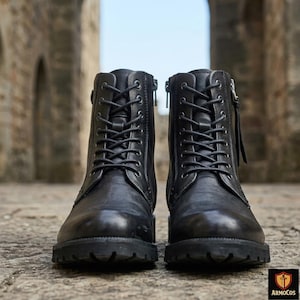 May include: A pair of black leather boots featuring a lace-up front with dark metal eyelets, a side zip closure with a leather pull tab, and a thick, textured rubber lug sole. The boots have a rounded toe and a structured ankle-high design.