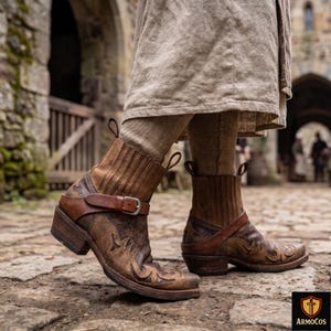 Peut inclure: Bottes de cheville en cuir marron avec surpiqûres décoratives et une bride à boucle. Les bottes ont un aspect vieilli et un talon épais. Les bottes font partie d'une tenue médiévale ou renaissance.