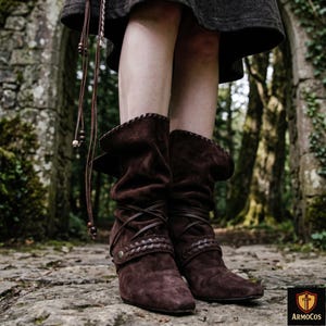 Peut inclure: Bottes en daim marron avec un dessus replié et des lanières de cuir entrecroisées. Les bottes ont un petit talon et des coutures décoratives sur le dessus. Elles font partie d'un costume médiéval ou de la Renaissance.