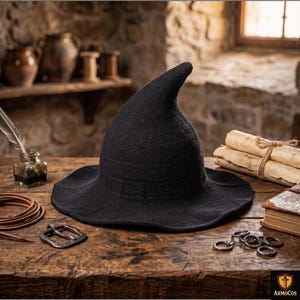 Peut inclure: Un chapeau pointu noir avec un large bord légèrement ondulé et une construction en tricot texturé. Le chapeau présente une couronne conique structurée qui se courbe légèrement au sommet. Le design inclut un détail de bande subtil.