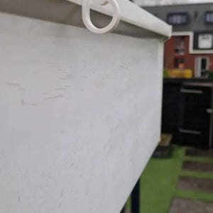 May include: A white gutter hook featuring a curved, scroll-like design at the end. The hook is securely attached to the top edge of a white gutter, providing a functional mounting point for hanging items along the exterior of a building structure.