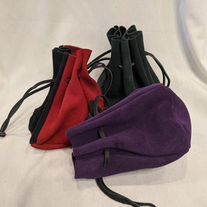 May include: Three drawstring pouches made of suede in red, purple, and green. The pouches have black leather drawstrings and are perfect for holding small items.