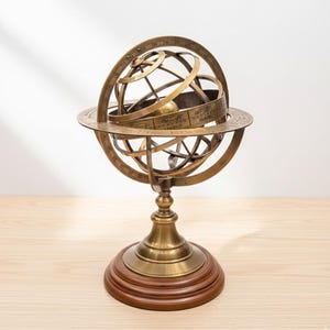 Könnte beinhalten: Eine Messing-Armillarsphäre, ein Himmelsmodell, steht auf einem Holzsockel. Die Sphäre hat mehrere miteinander verbundene Ringe, die Himmelskreise darstellen. Der Sockel ist aus dunklem Holz und die Sphäre hat eine polierte, antike Oberfläche.