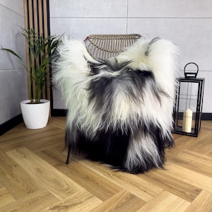 Peut inclure: Une peau de mouton à poils longs présentant un motif dégradé passant du blanc en haut au noir en bas. La texture épaisse et hirsute de la fourrure recouvre l'assise et le dossier d'une chaise en rotin tressé, créant un aspect doux et superposé.